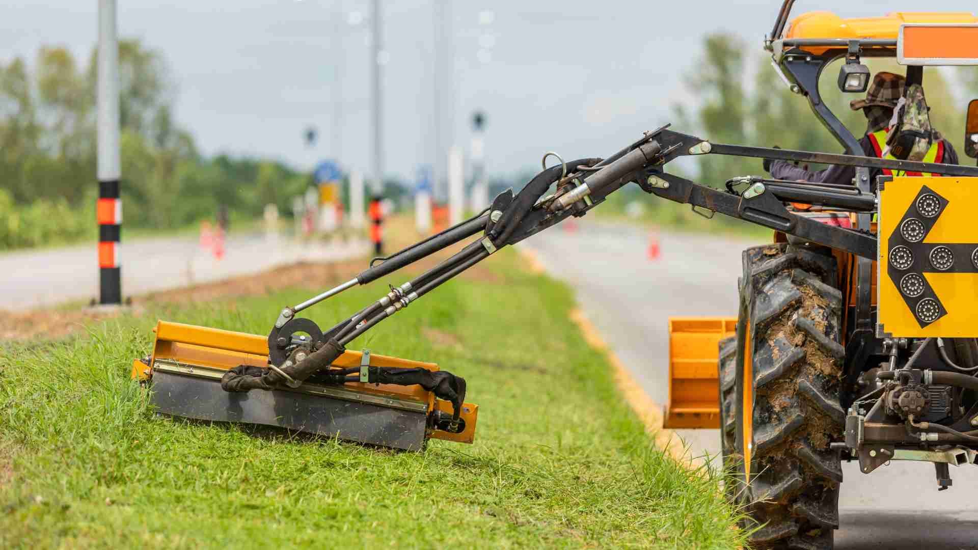 Yellow industrial lawn mower mowing grass on the side of a road