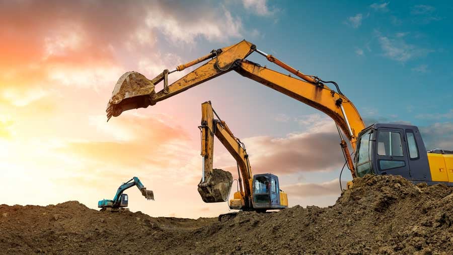 Three yellow machines on dirt mounds working