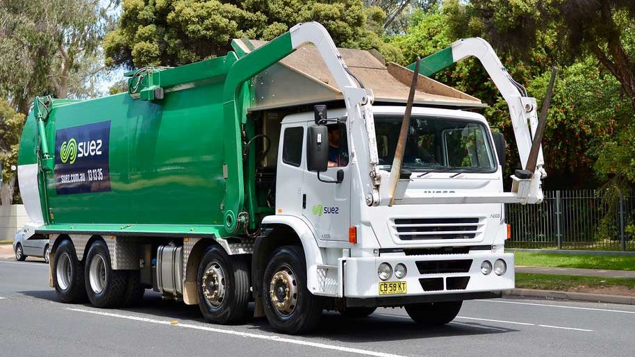 Green Suez garbage truck driving on road