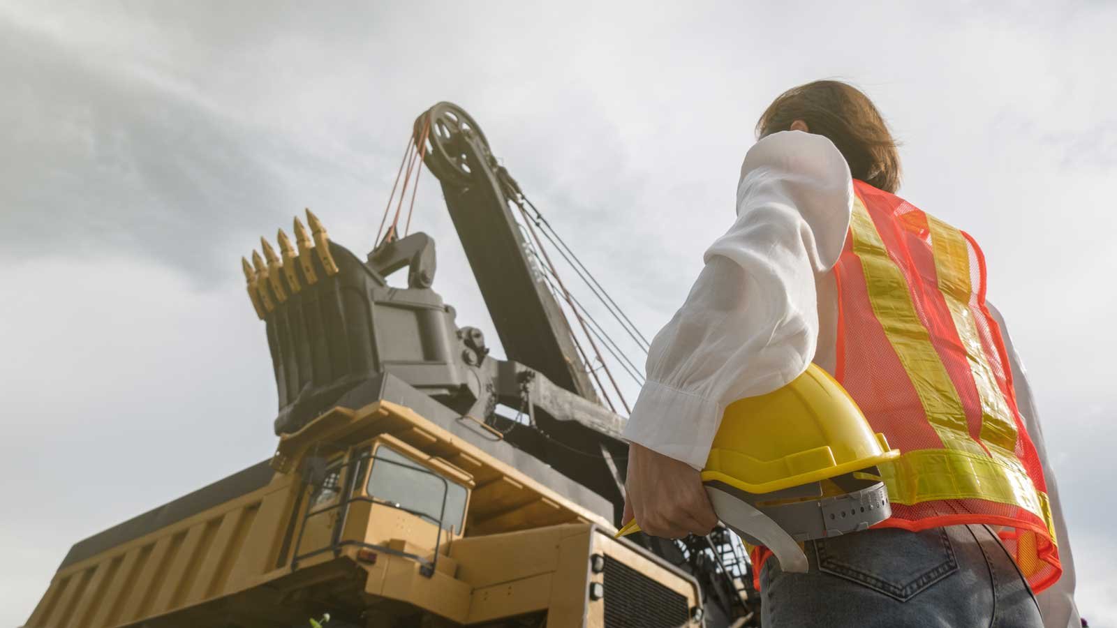 Man looking up at machine holding hard hat on his waist
