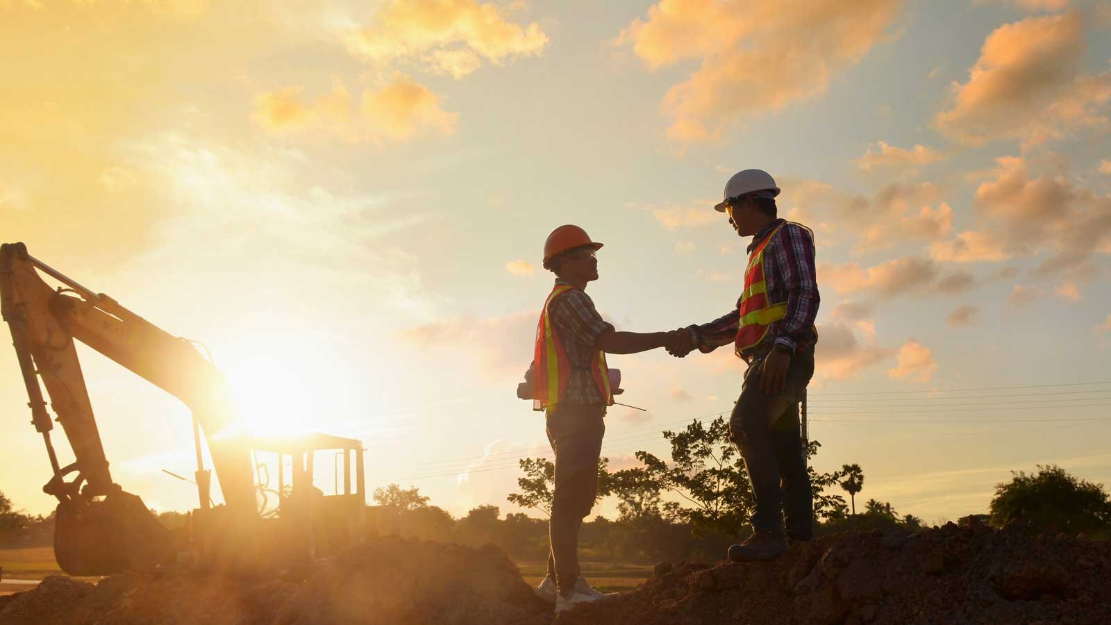 Two construction workers shaking hands with machine in background