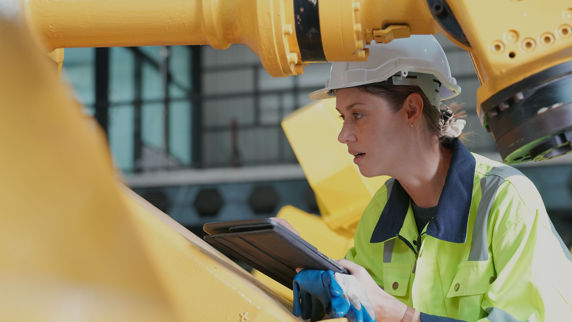 Close up of a woman wearing safety gear and a hardhat inspecting a yellow machine