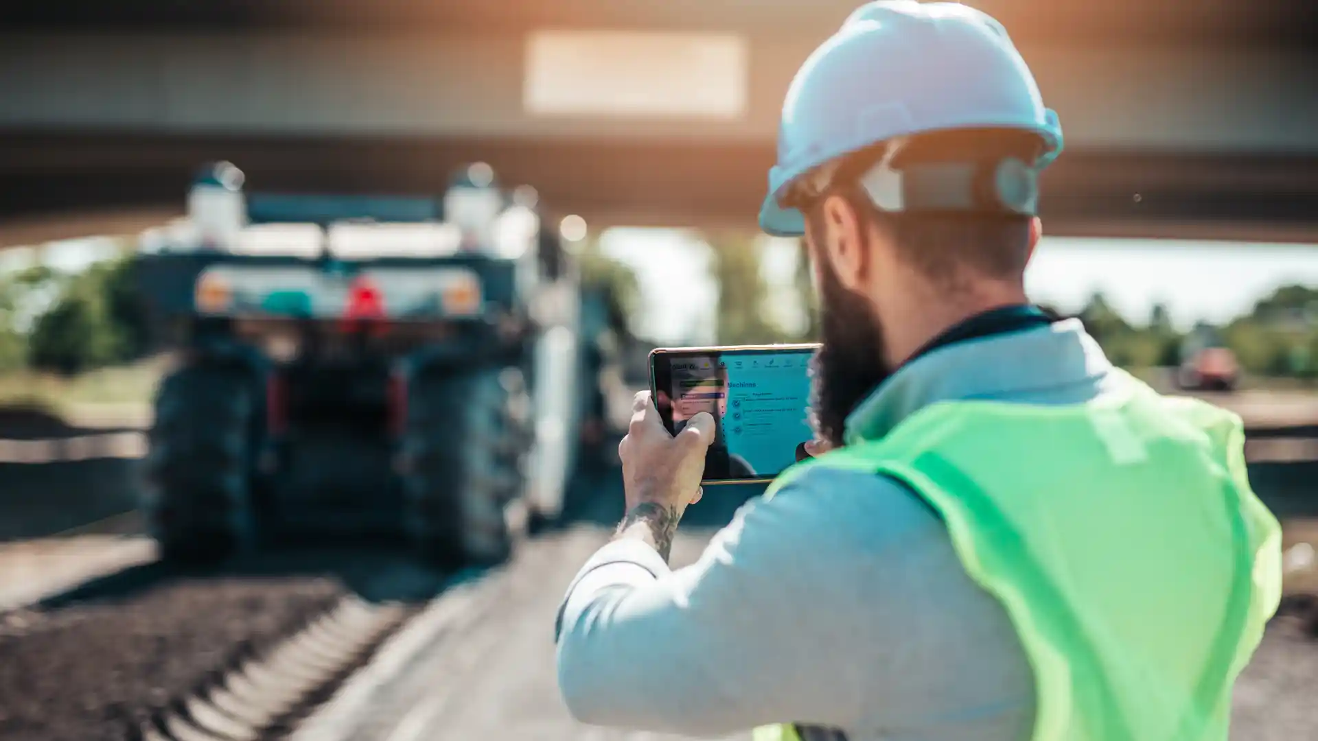 Close up of a worker wearing PPE and holding a tablet taking a photo of a piece of heavy machinery
