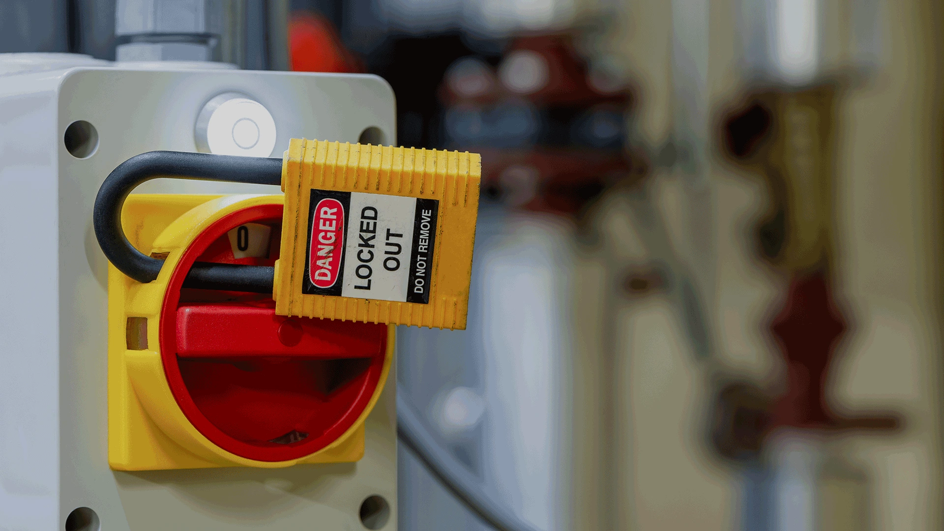 Yellow padlock with label saying danger locked out do not remove attached to a red and yellow switch on a machine