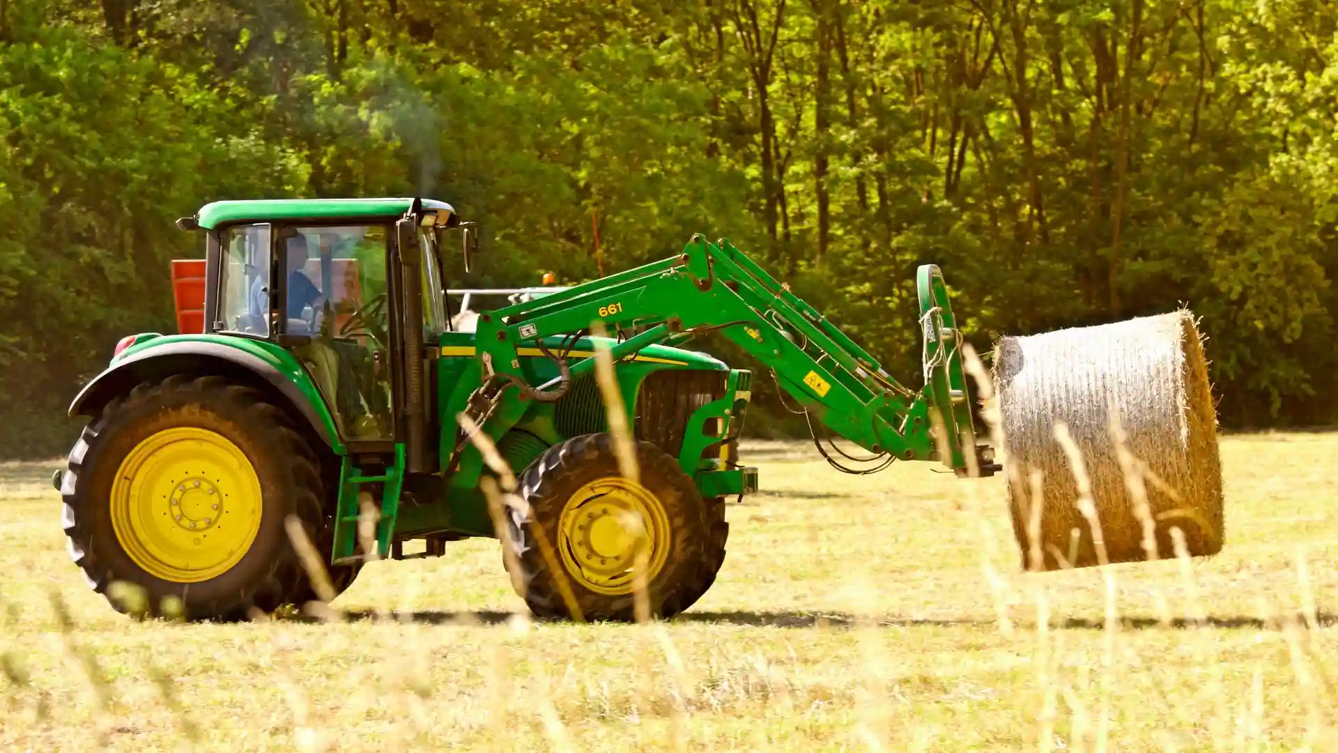 Green tractor transporting a bale of hay