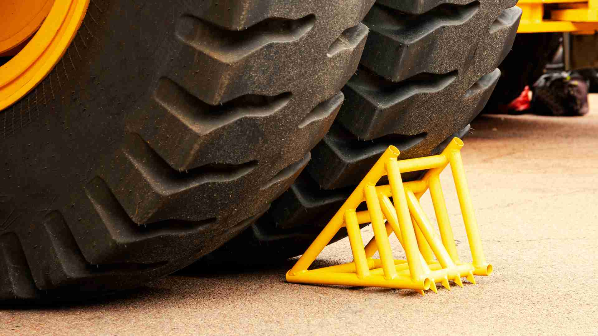 Close up of heavy machine's wheel with yellow wheel chock wedged underneath