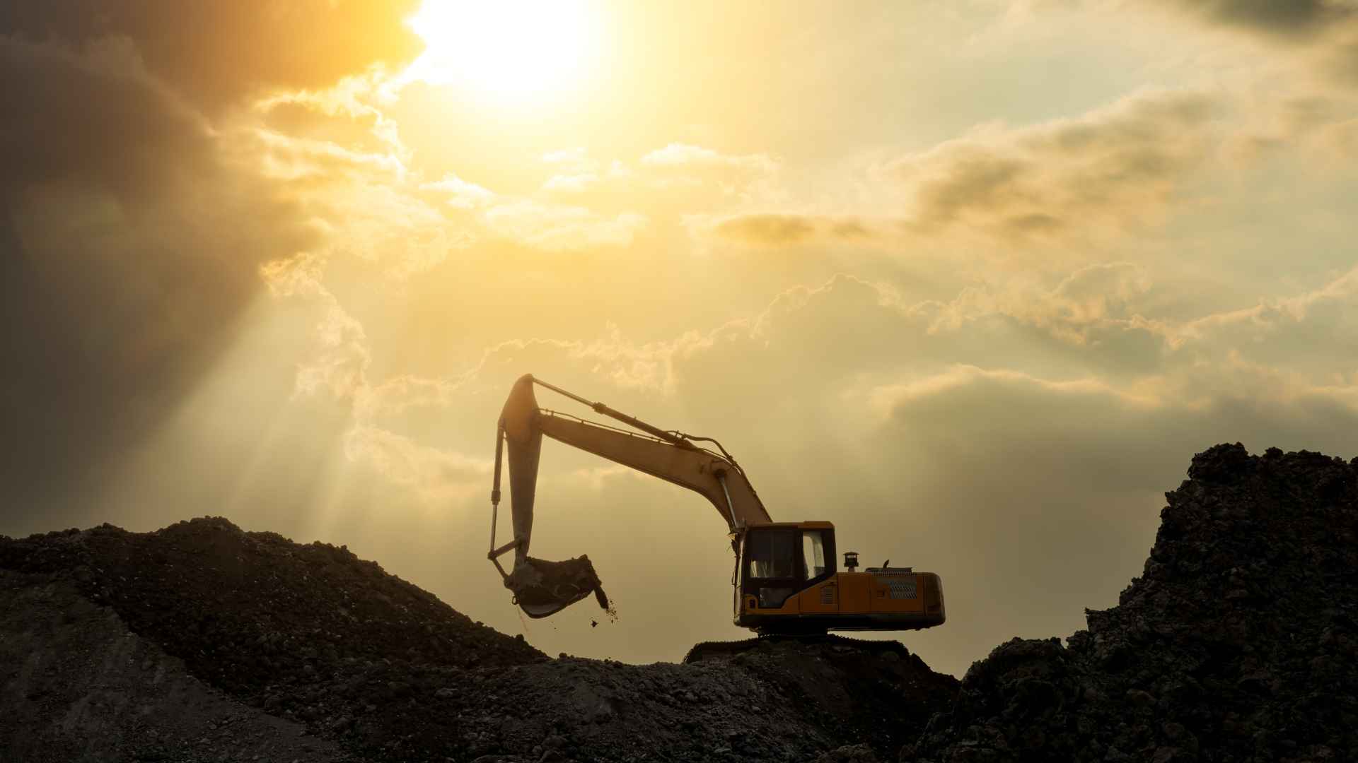 Yellow excavator working on site with sunset in the background