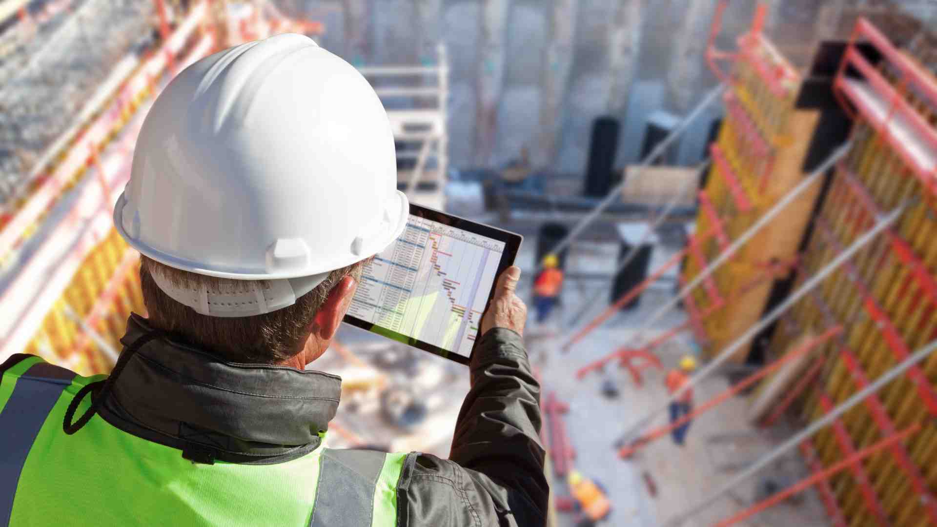 Person wearing protective gear and a hard hat using a tablet while looking over a construction site from above 