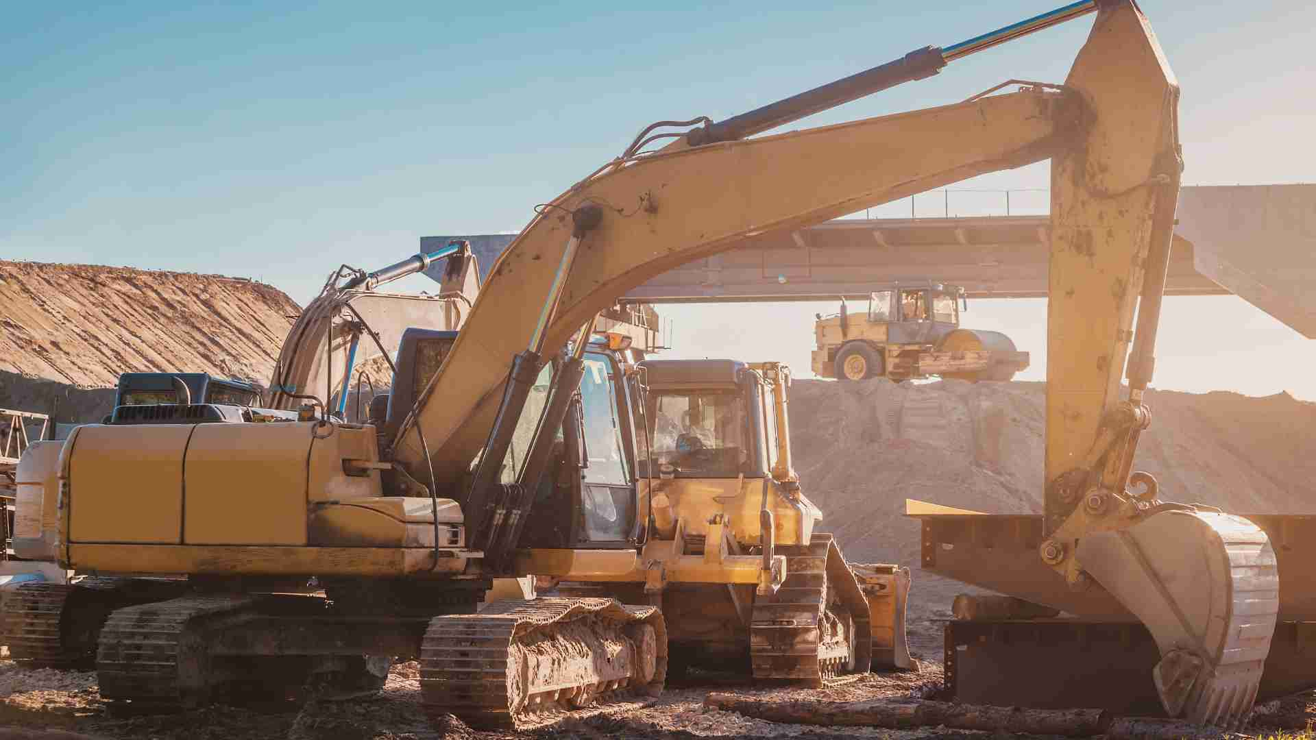 A variety of yellow heavy machinery on a dusty worksite