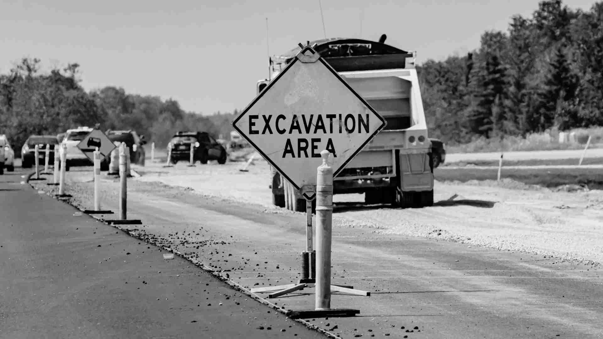 Black and white close up of an excavation area sign on a busy road