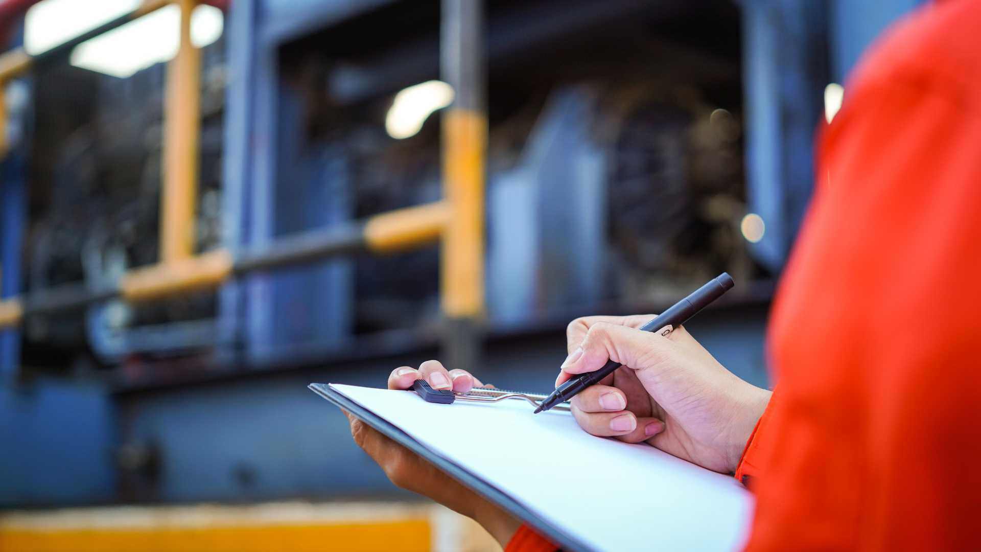Close up of a person holding a clipboard inspecting heavy machinery