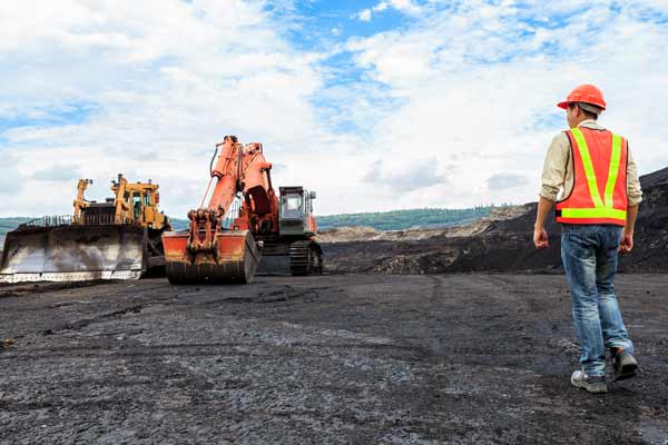 Man in hi-vis walking towards a fleet of heavy machinery on a work site