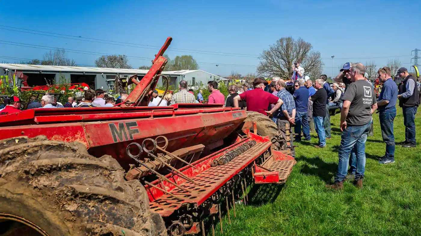 A rural auction with agricultural equipment and a crowd standing around watching