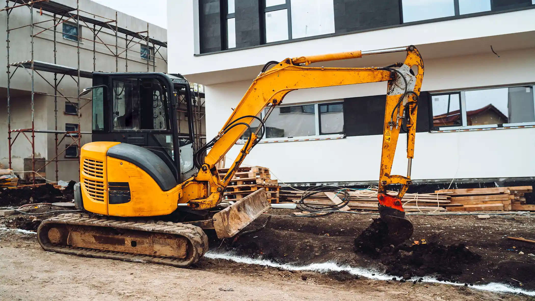 Small yellow excavator doing landscape work on house construction site