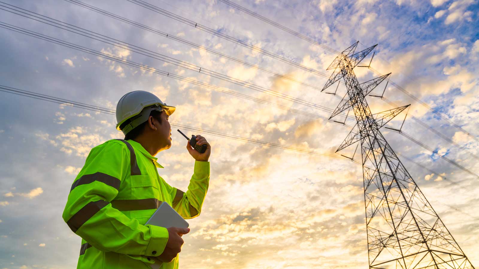 Man in high vis with radio looking up at powerline utilities