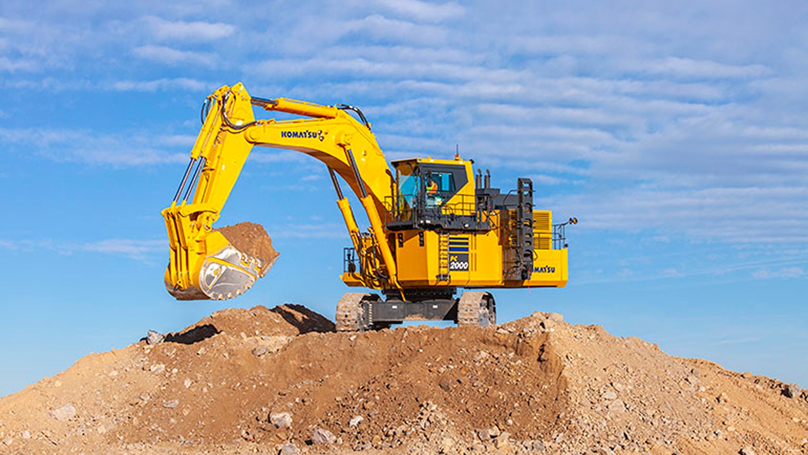 yellow hydraulic excavator on top of dirt mound